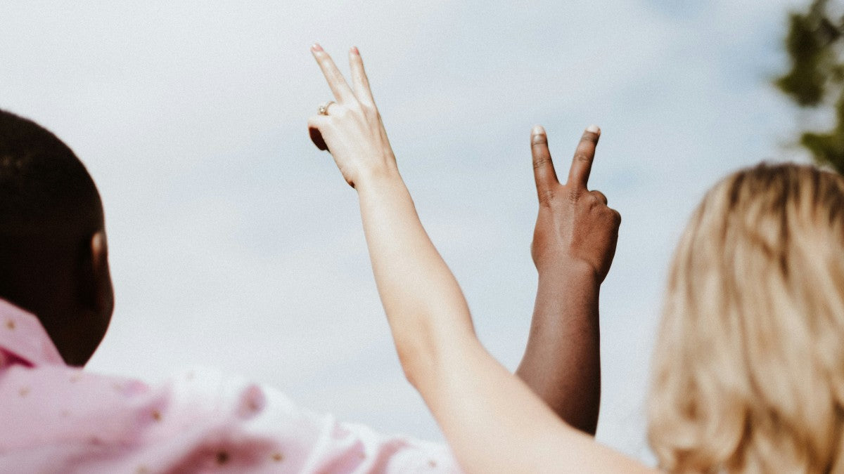Two people making peace signs with their hands against a light blue sky.