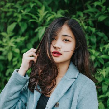 Woman with long dark hair standing against a green leafy background