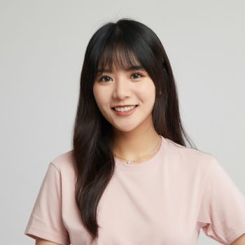 Woman with long dark hair wearing a pink shirt against a plain background