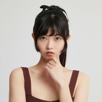 Woman with black hair tied back, wearing a brown top, against a plain background